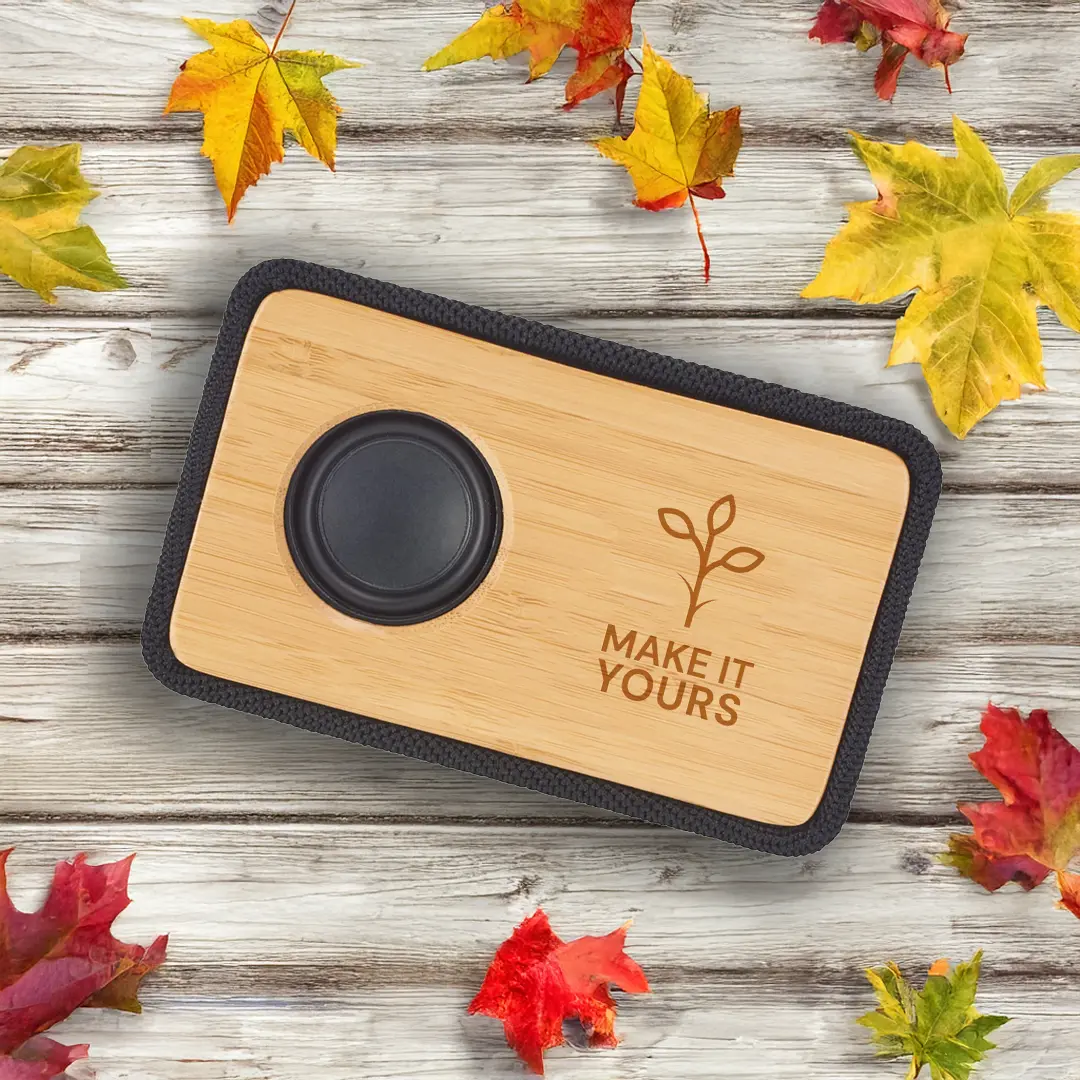 bluetooth speaker laying on wooden table surface and surrounded by autumn leaves