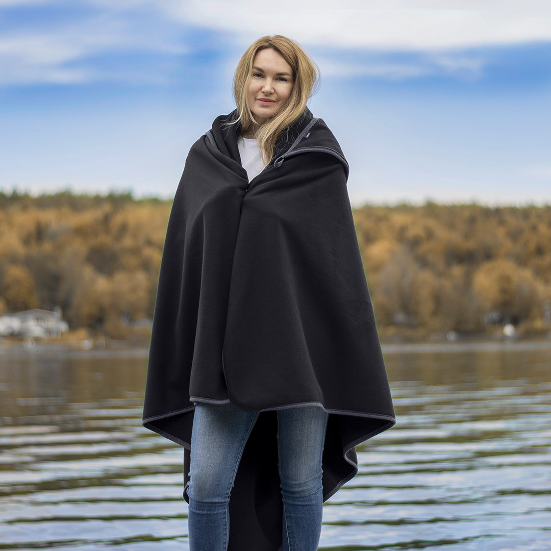 woman standing by a lake wrapped in cozy blanket and smiling