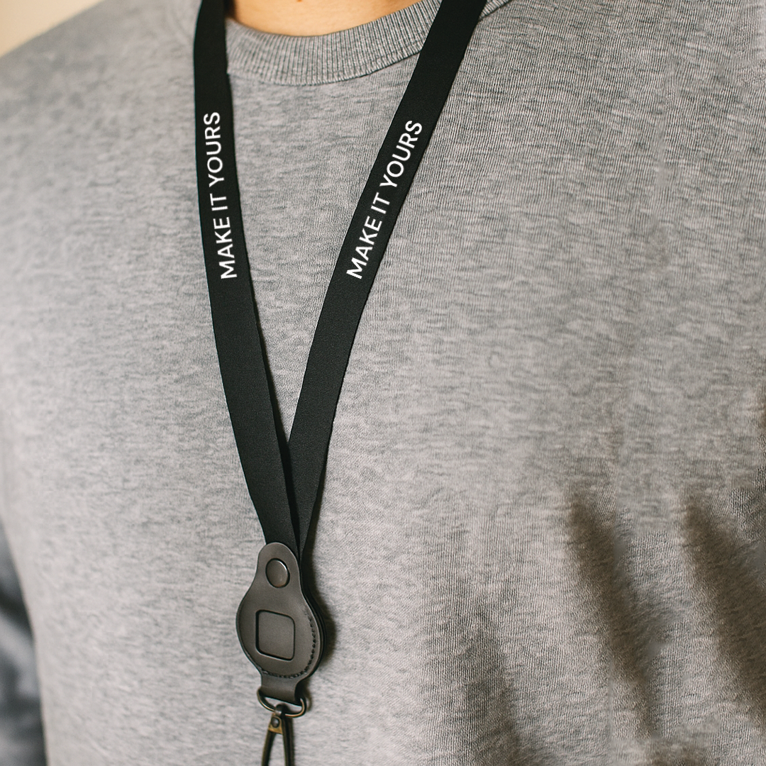 man wearing grey sweater and black airtag lanyard around neck