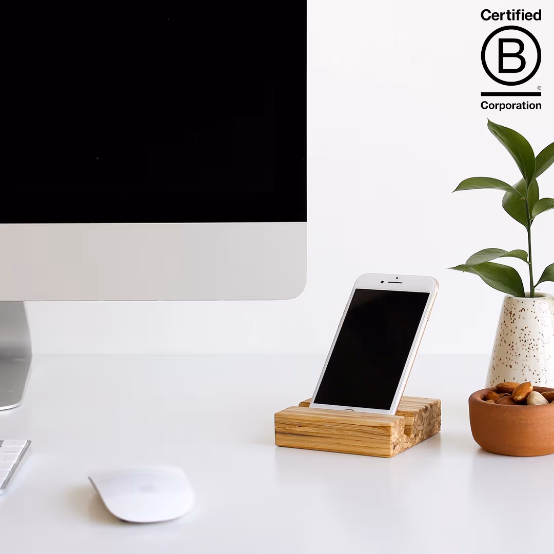 clean white desk with bamboo phone stand resting beside potted plant and computer