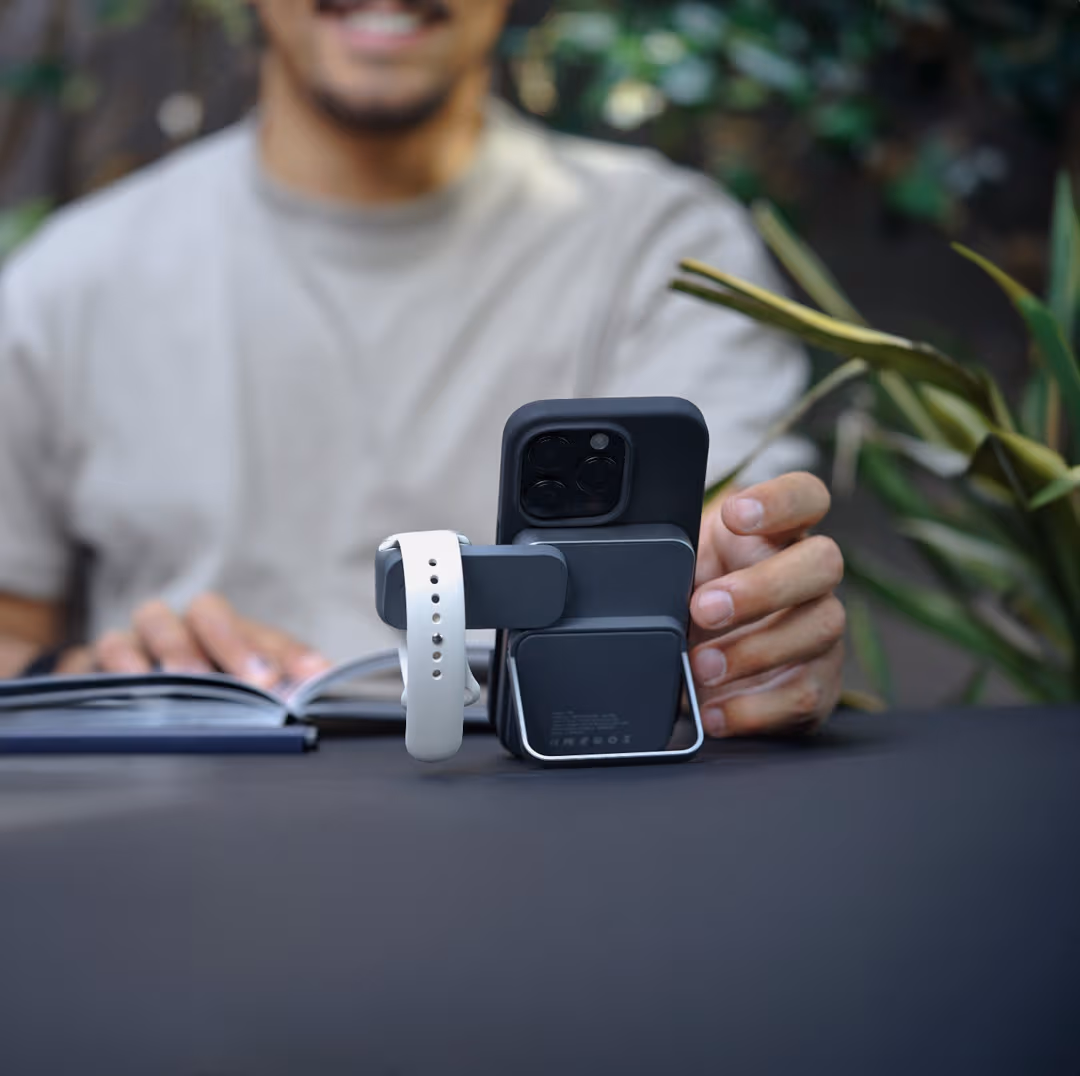lifestyle image of man sitting at table reading from a book with his phone propped up on the wireless power bank as it charges his phone and his smartwatch
