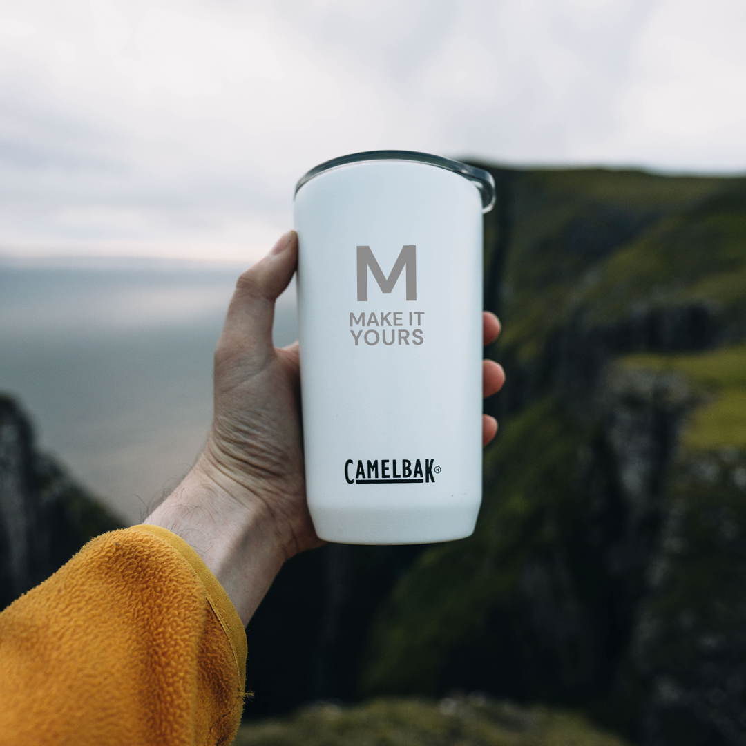 white tumbler being held in someone's hand with a mountain range in the background