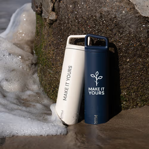 two water bottles resting against a rock at the beach with the tide coming in