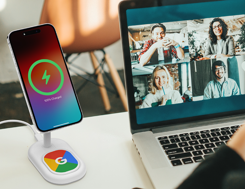 wireless phone charging stand on computer desk beside laptop where remote team meeting takes place